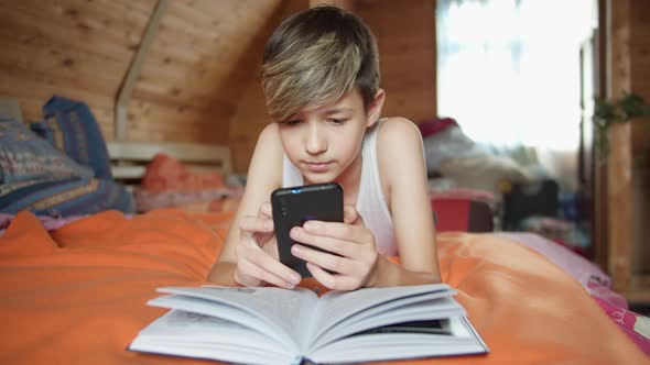 boy lies on the bed pretends to read a book but uses the phone