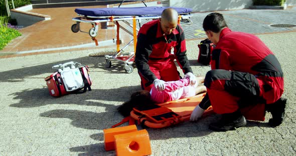 Paramedics putting injured girl onto a backboard alt