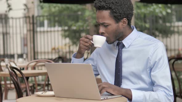 African Businessman Working on Laptop and Drinking Coffee, Outdoor Cafe alt