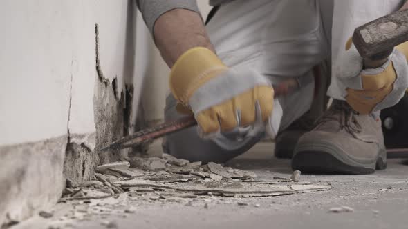 Construction worker hands with gloves working with hammer and chisel to remove old plaster from wall
