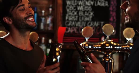 Two male friends interacting with each other while toasting a beer bottles alt