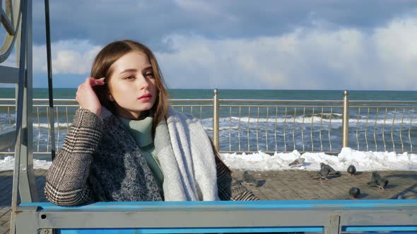 A Woman Wearing a Coat is Sitting on a Swing on the Promenade alt