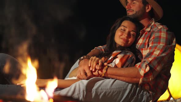Man Hugging Woman in Front of the Bonfire on Beach Party in the Dark alt