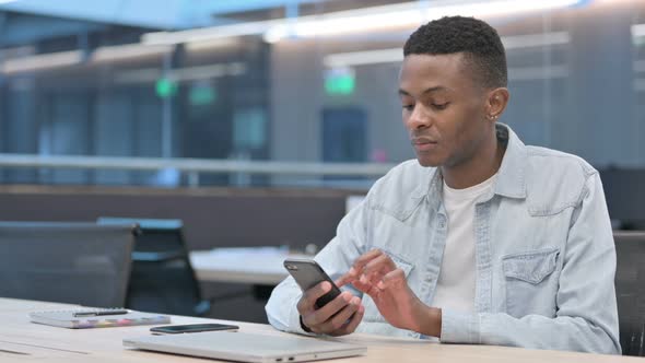 African Man Celebrating Success on Smartphone in Office alt