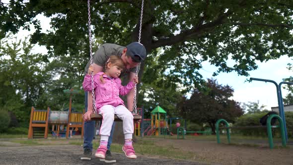 Happy Little Daughter is Having a Good Time on the Playground with Her Loving Dad