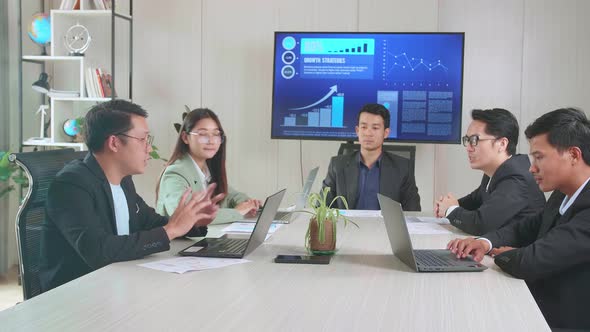 Young Asian Team Have Meeting In A Conference Room. They Share Opinions, Statistics Show On Tv alt