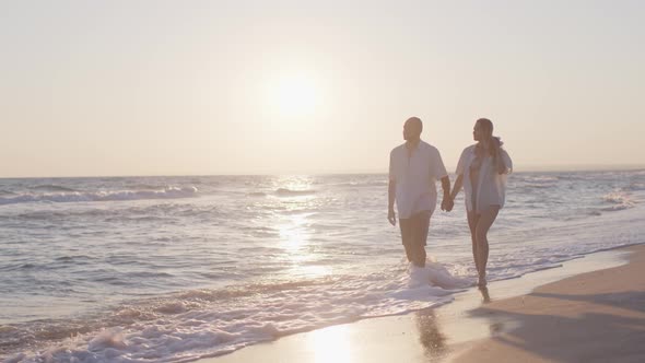 Couple of Young Lovers Holding Hands Walking Along the Beach By the Sea
