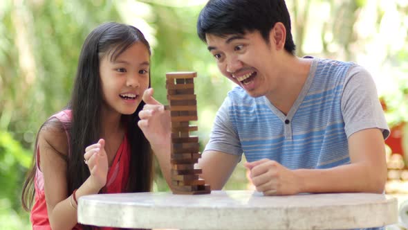 Asian girl playing a game of risk trying to move wooden blocks with father. alt