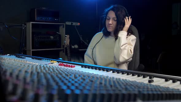 a Young Girl Wearing Headphones Sitting in a Music Studio at a Large Mixer and Nodding Off to Music