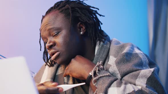 Worried and Ill African American Black Man with High Fever Having Video Call Using Laptop alt