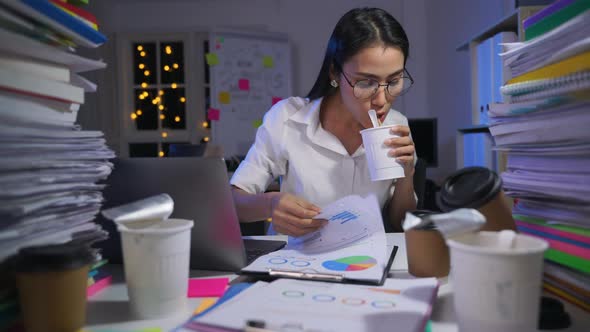 business woman is sitting at desk cover with stack of paperwork and eating