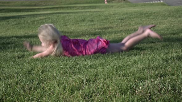 Happy Baby Girl Slides Down the Grass From a Green Hill in the Park alt