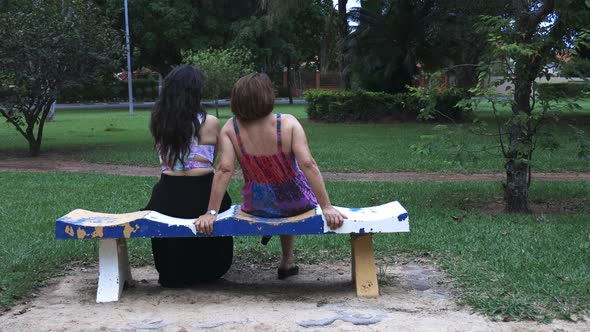 Mother and daughter sitting on a bench in the park talking to each other and chilling down alt