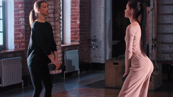 Two Skinny Women Training Together in the Gym  Squatting with a Dumbbell in Front of Each Other alt