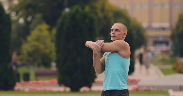 Handsome Young Man Stretches the Muscles of the Arms Training Outdoors in the Summer