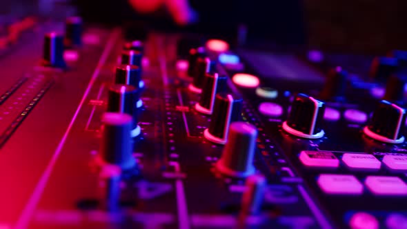 Closeup of Dashboard Mixing Console Illuminated By Neon Buttons of Which are Pressed By DJ Hand alt