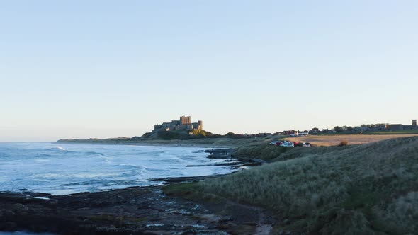 Aerial establishing shot of Bamburgh Castle and coastline during sunset alt