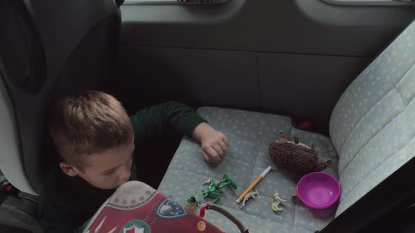 A boy sitting on a cars floor playing with some toys on a back seat alt