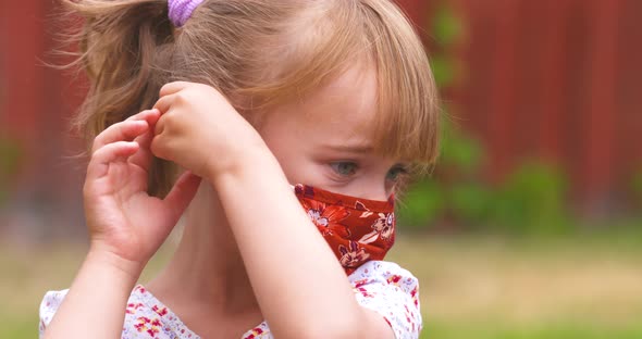 Sweet little girl putting on her face mask to protect against coronavirus. alt