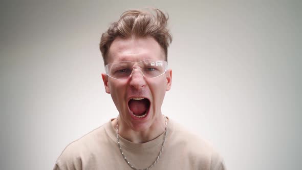 Funny Angry Man in Glasses Looks at the Camera and Screams on a White Background alt