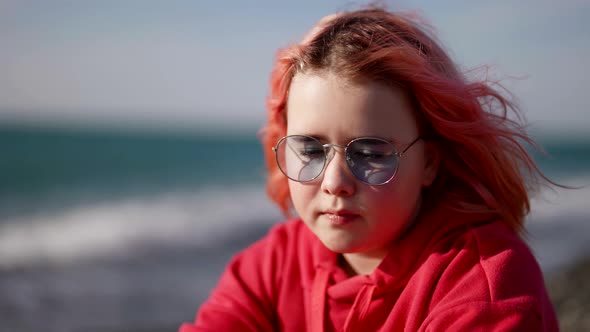 Little Girl with Pink Hair is Sitting on Seashore Cute Child on Beach in Spring Windy Day alt