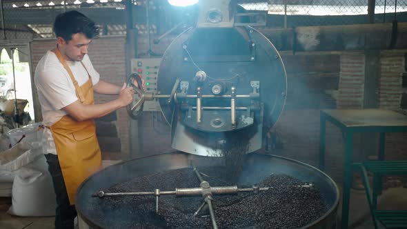 Young man pouring coffee roasted from the oven in his own factory, smoke is rising due