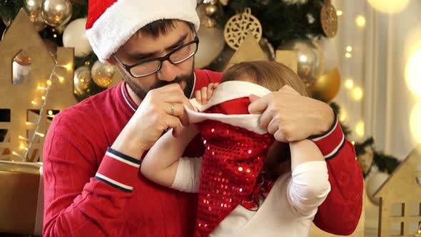 Father with Child Girl Dress Red Santa Hat Smile and Laugh on Background of Christmas Tree