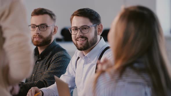 Young Happy Business Partners Talking and Smiling Behind Modern Office Table at Meeting, Listening alt