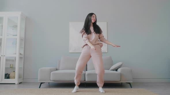 Millennial girl with glasses in pink casual home wear happily dancing  jumping.