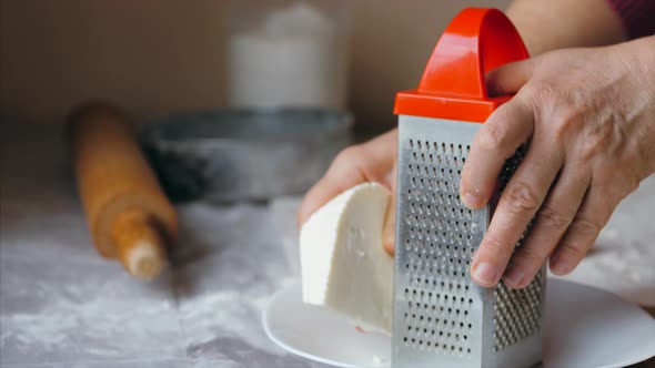 Close-up hands of mature woman is rubs a cheese on a steel grater