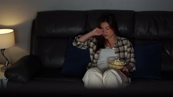 sad young woman watching television and crying on sofa at night