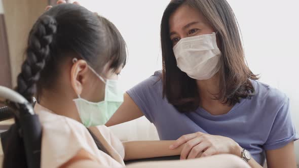 Asian beautiful loving mother take care of kid with love on wheelchair in recovery room in hospital. alt