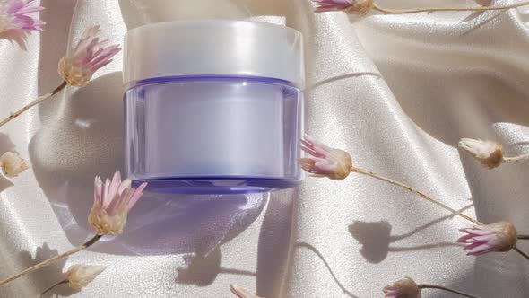 Blue glass cream jar mockup on smooth silk fabric sunlight flowers shadow water splashes Skincare 4K alt
