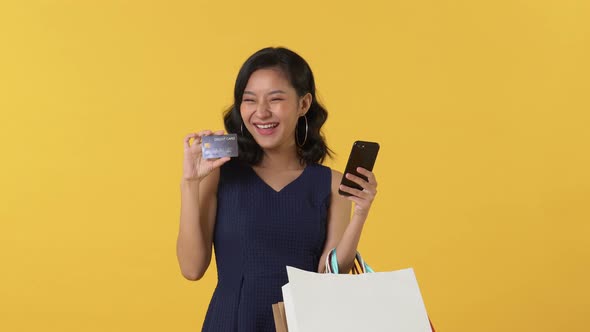 Beautiful smiling Asian woman shopping online with mobile phone and paying with credit card