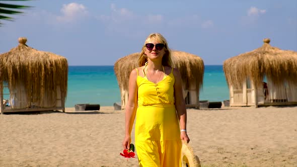 A Woman in a Hat and Dress Walks on the Beach alt