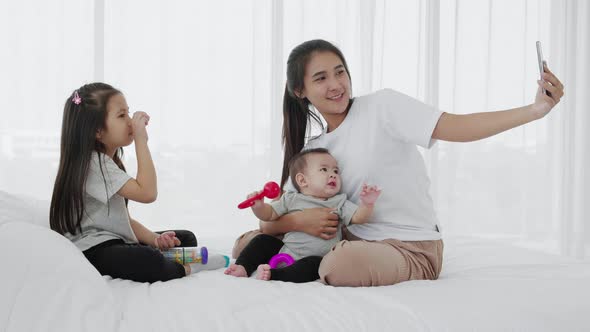 mother, daughter, baby use smartphone selfies together on bed, Slow motion