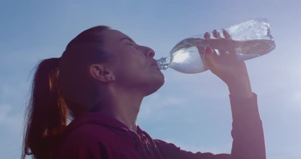 Sweating Fitness Female Is Drinking Water From A Bottle After Sports With Backlit Sun And Blue Sky alt