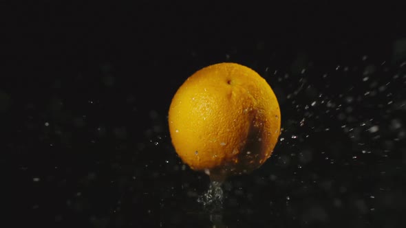 Orange Falls In Water In Dark And Splashes Scatter In Different Directions