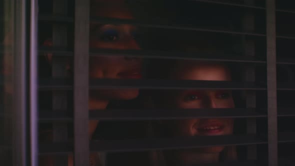 Two girls openong shutters and looking through the window and smiling alt