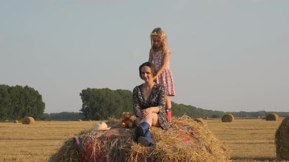 Little Girl Doing Hair of Her Mother on Hay Bale alt