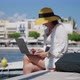 Mature Woman in a Hat with a Laptop on the Sea Promenade in the City - VideoHive Item for Sale