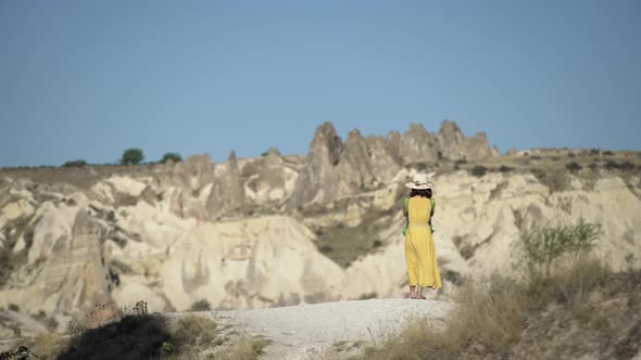 A female tourist is looking at Cappadocia on the mountain in the middle.