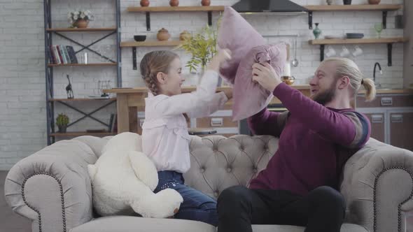 Joyful Caucasian Father and Daughter Sitting on Couch and Fighting with Pillows, Cheerful Man alt