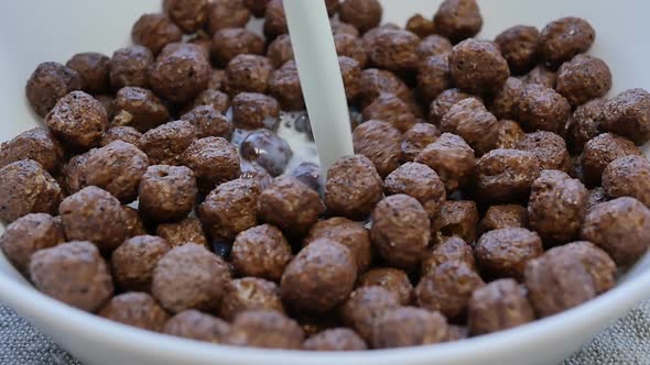 a Stream of Milk is Poured Into a Bowl with Dry and Crunchy Cocoa Balls