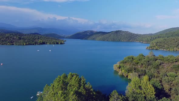 Aerial view of the lake surrounded by many green trees with mountains in the background alt
