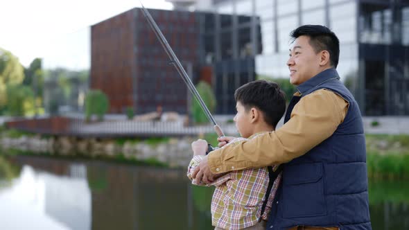 Asian Father Teach His Son How to Cast a Fishing Rod Correctly From the Pier alt