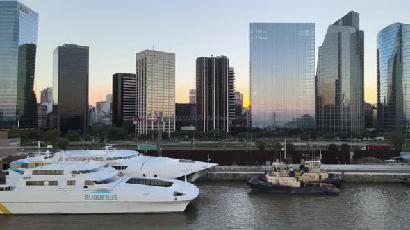 Aerial dolly right of boats parked in Puerto Madero docks with skyscrapers in background at sunset, alt