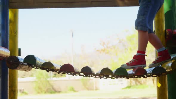 Boy climbing an small wooden hanging bridge on the playground alt