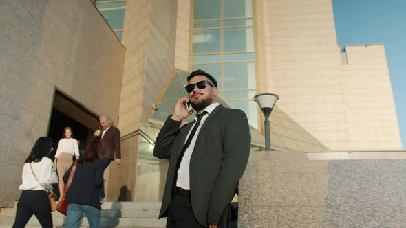 Joyful Businessman Enjoying Corporate Conversation on Mobile Phone Standing Near Office Center alt
