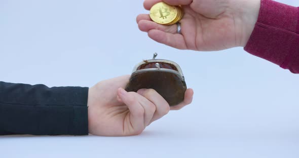 Male Hand Puts a Cryptocoin Bitcoin or BTC in a Small Brown Wallet Depicting Earning or Paying with alt